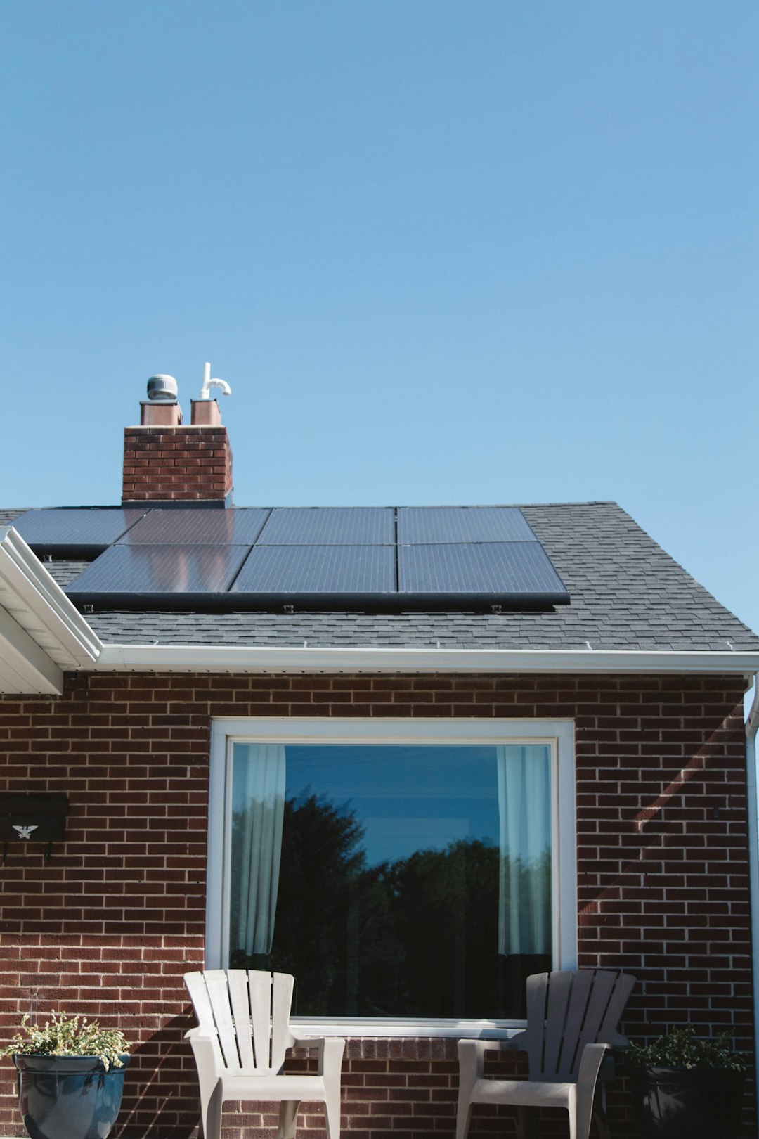 about-img Vivint Solar - Solar Panels on roof of brick home with window and Adirondack chairs.